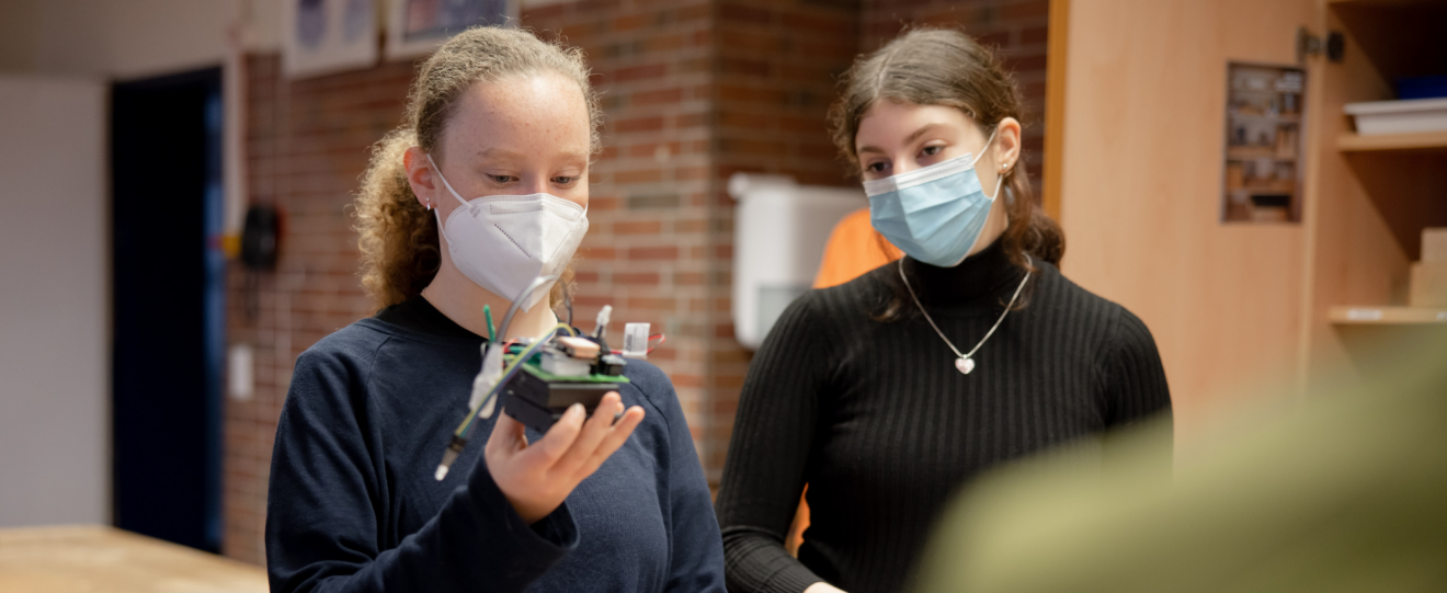 zwei Mädchen mit Mundschutz hält ein elektrisches Gerät in der Hand